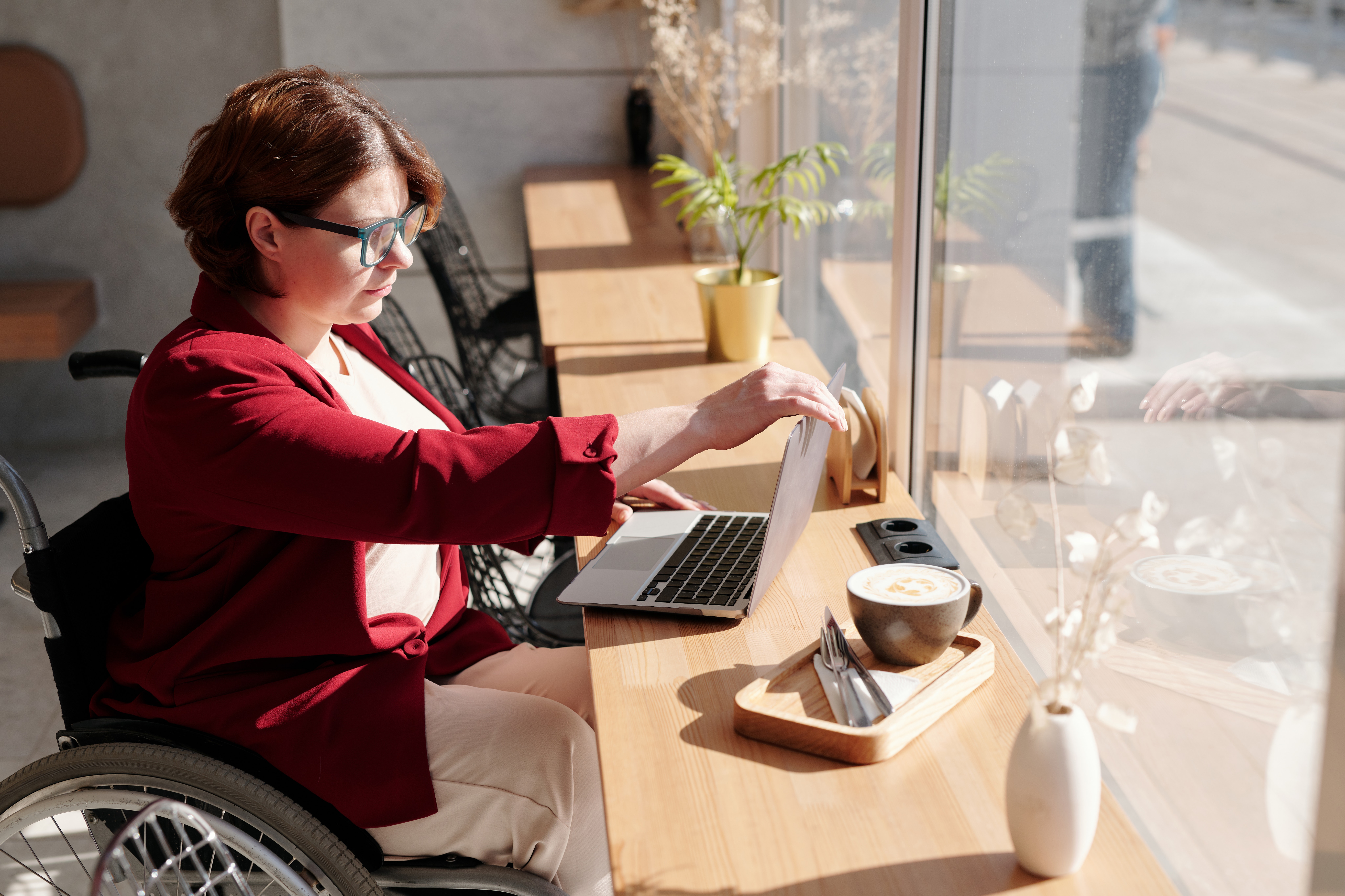 woman in a wheelchair using laptop and drinking coffee